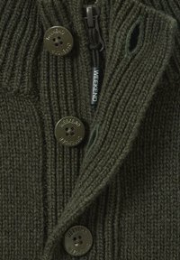 Dunkelgrüner Strickstoff mit drei Knöpfen, die mit "Weekend Offender" graviert sind, und einem schwarzen Reißverschlussanhänger mit der Aufschrift "WEEKEND".
