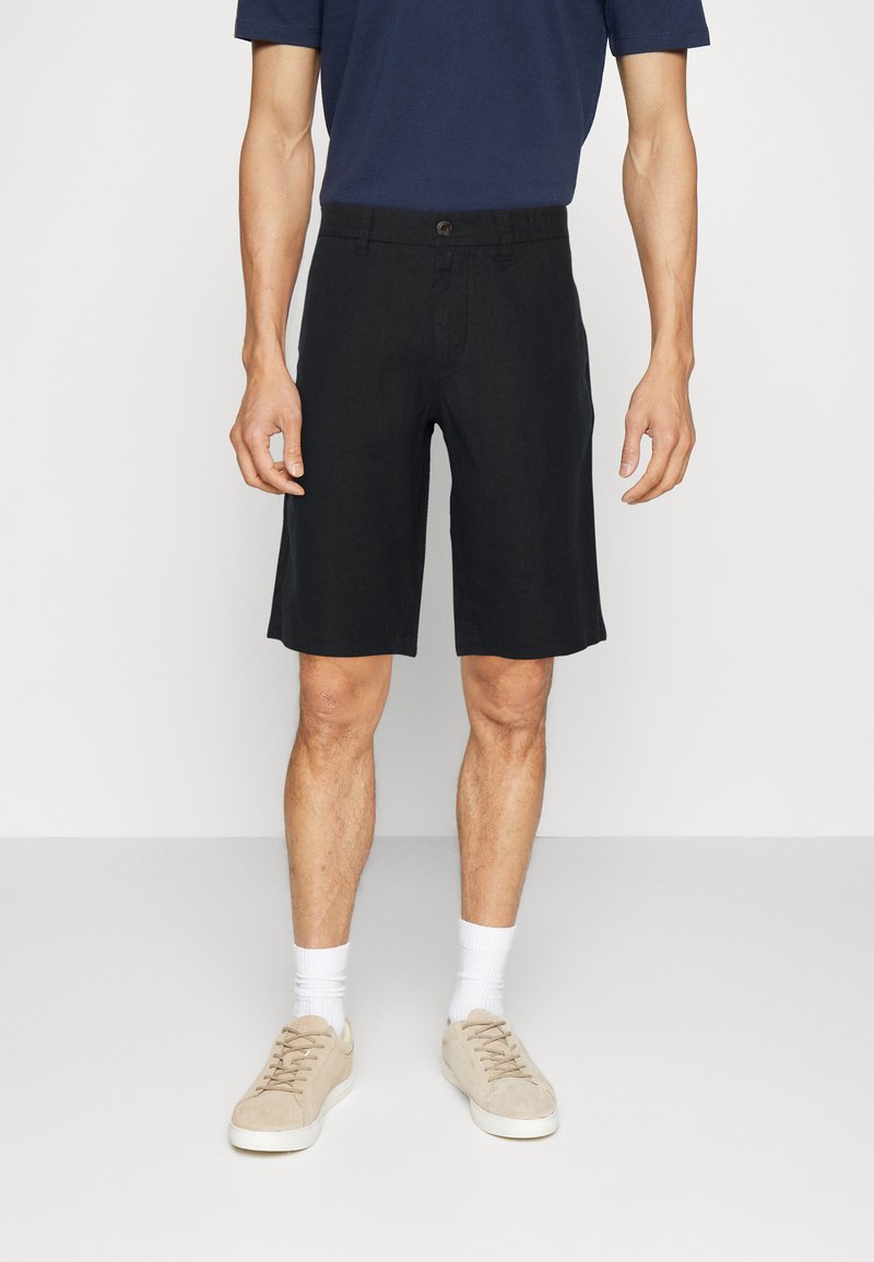 Schwarze Leinen-Shorts mit geradem Schnitt und Knopfverschluss. Getragen mit einem dunkelblauen Hemd und beigen Sneakern, ergänzt durch weiße Socken.