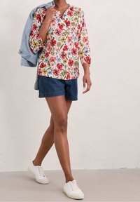 Camicia a maniche lunghe a fantasia floreale bianca con fiori rossi, rosa e blu; abbinata a pantaloni corti in denim scuro e sneakers bianche, giacca in denim chiaro.