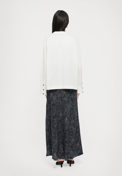White long-sleeve blouse with a collar and button accents, paired with a dark floral-patterned maxi skirt and black heeled sandals.