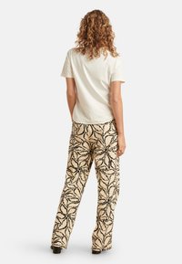 Witte katoenen t-shirt gecombineerd met beige wijde broek met een zwart bladerenpatroon, een soepele textuur en een ontspannen pasvorm.