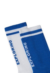 Bawełniane skarpetki o prążkowanej fakturze; jedna biała, a druga niebieska. Obie mają na boku nadrukowane wyraźne białe litery "EXPLORING".