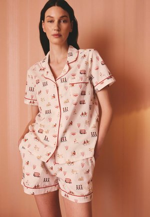 Žena má na sobě krémově zbarvený krátký pyžamový set s červeným lemováním a motivy Londýna, včetně strážců, autobusů, psů a korun.