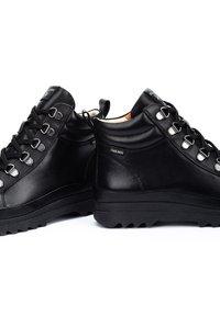 Bottines en cuir noir avec une texture lisse, œillets en métal, lacets ronds et une semelle en caoutchouc robuste avec un bord denté.