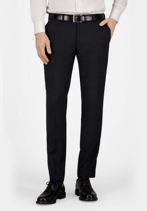 Mann trägt schwarze Anzughose, schwarzen Ledergürtel, schwarze polierte Anzugschuhe und ein weiß gestreiftes Langarmhemd.