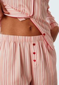 Rosa randig pyjamaset med röda detaljer, med en knäppt midja och resårmidja; mjukt tyg med en slät textur.