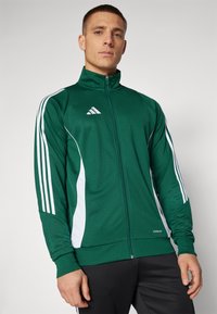 Grønn zip-up treningsjakke med hvite detaljer, med tre vertikale striper på hver arm. Laget av glatt stoff, har den høy krage.