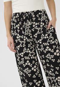 Pantalons floraux noirs à coupe ample, dotés d'une taille élastique avec cordons de serrage et d'un motif de fleurs blanches avec des accents rouges. Tissu léger et texturé.
