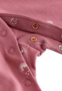 Tissu en coton rose avec boutons-pression, présentant des accents métalliques en or rose, argent et un motif arc-en-ciel multicolore. Texture lisse.