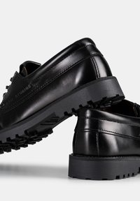 Scarpe in pelle nera con punta arrotondata, suola texturizzata e dettagli di cucitura minimi, dotate di battistrada pronunciato per una buona aderenza.