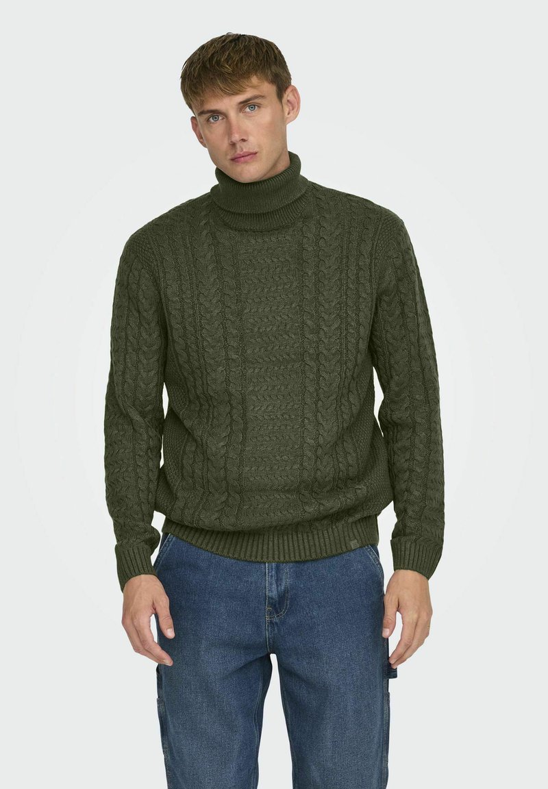 Suéter de punto verde oliva con cuello alto, que presenta un patrón de trenzado texturizado y puños y dobladillo acanalados, combinado con jeans azules.