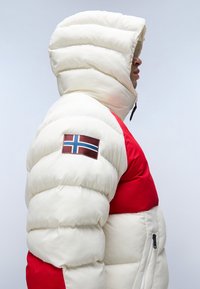 Giacca imbottita con una combinazione di colori bianco e rosso, dotata di un grande cappuccio, texture a coste e un patch della bandiera norvegese sulla manica.