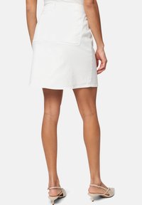 Jupe en denim blanc avec une taille ajustée, forme en A et deux poches arrière. Le tissu semble léger avec une texture lisse.