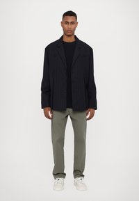 Navy-gestreifter, oversized Blazer, kombiniert mit einem navyblauen, strukturierten Rundhalsausschnitt-Pullover, olivgrünen Hosen und weißen Sneakers.
