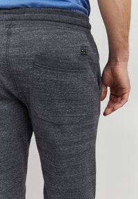 Tamne sive trenirke od mekog, strukturiranog materijala s stražnjim džepom i malim crnim logom. Elastični pojas za udobnost.