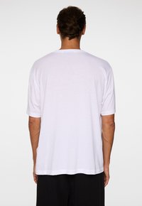 Vit bomulls t-shirt, korta ärmar, avslappnad passform, enkel design, rundad halsringning, med rak nederkant. Sedd från baksidan.