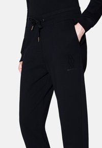 Pantaloni della tuta neri realizzati in tessuto morbido, con vita elasticizzata, chiusura con cordino e dettaglio del logo discreto sulla gamba.
