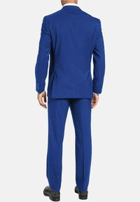 Costume bleu à la coupe ajustée, fente simple à l'arrière et pantalon droit. Le tissu semble lisse avec une texture minimale. Chaussures noires.