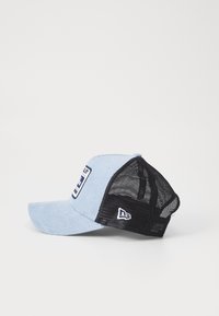 Gorra trucker de pana azul con parte trasera de malla negra, que presenta un parche en la parte frontal y un logo en el lateral. Visera curva, ajuste ajustable.
