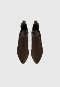 Bottines en daim marron avec bouts pointus, fermetures éclair latérales et languettes de tirage. Semelles plates et doublure intérieure lisse. Design épuré et minimal.