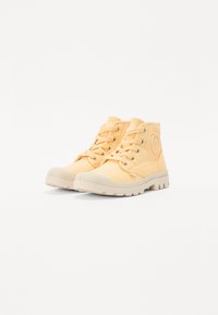 Pantofi canvasa galbeni, tip high-top, cu talpă din cauciuc crem, vârf rotund, șireturi și patch cu logo pe lateral. Material texturat și design robust.