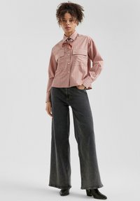 Chemise à rayures roses à manches longues avec deux poches poitrine, associée à un jean noir à taille haute et à jambes larges, ainsi qu'à des bottes noires à talons.