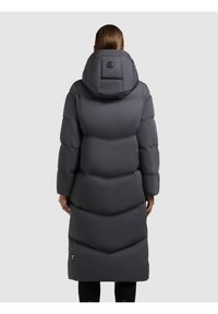 Dlouhý šedý péřový kabát s kapucí, který má horizontálně prošívané části, logo na zadní straně a rovný střih.