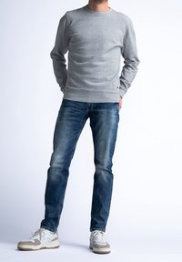 Světlě šedá mikina s kulatým výstřihem a žebrovanými lemy, doplněná tmavě modrými džínami a bílými teniskami s šedými detaily.