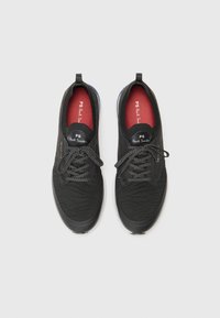 Černé pletené tenisky s texturovaným svrškem, kulatou špičkou, šněrováním, kontrastní červenou stélkou a jemným logem značky.