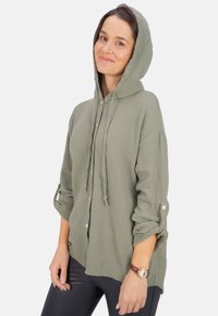 Leichte, olivgrüne Kapuzenshirt mit strukturiertem Finish, Knöpfen, hochrollbaren Ärmeln und lässiger Passform. Mit einer Kordelzugkapuze.