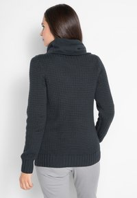 Maglione a maglia grigio scuro con colletto alto, motivo testurizzato e polsini a costine. Il design sul retro è aderente e semplice, senza decorazioni.