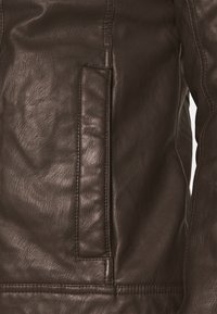 Giacca in pelle marrone con una texture liscia, cuciture verticali e una tasca laterale. Il materiale presenta una grana e una lucentezza naturali.