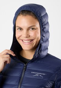 Navy puffer jacket with a quilted design, featuring a hood and zipper front. The logo "SWEDEMOUNT" is visible on the chest. Smooth texture.