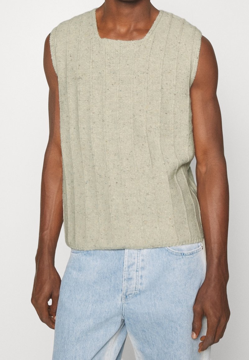 Jersey sin mangas de color verde claro con textura de canalé vertical. Corte holgado, escote redondo y manchas visibles de material más oscuro.