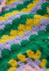 Primo piano di tessuto lavorato a uncinetto colorato con motivi a zigzag in filati verde, giallo, viola e rosa.