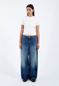 White short-sleeve top paired with wide-leg blue denim jeans featuring a faded finish, large pockets, and a button closure at the waist.