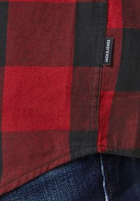 Ourlet de chemise à carreaux rouge et noir avec étiquette « JACK & JONES » au-dessus d'un jean en denim bleu foncé.