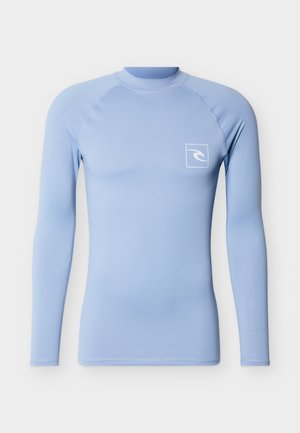 Rash guard à manches longues bleu clair avec un petit logo vague blanc sur le côté gauche de la poitrine, conçu pour les sports nautiques.