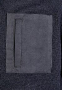 Marine gebreide stof met een groot, vierkant, donker suède patch en een rechthoekige slit pocket. Stiksel is zichtbaar rond de suède details.
