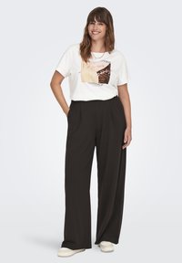 Camiseta blanca con estampado gráfico combinada con pantalones negros de pierna ancha y cintura alta. El modelo lleva zapatillas de colores claros.