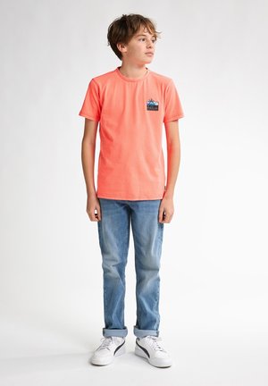 Koraalkleurig T-shirt met korte mouwen, voorzien van een klein logopatch op de borst. Gekocht in combinatie met lichtblauwe jeans en witte sneakers.