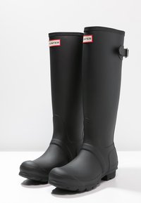 Schwarze Gummiregenstiefel mit glänzender Oberfläche, hohem Design und silbernem Schnallendetail an der Seite. Verfügt über strukturierte Sohlen für besseren Halt.