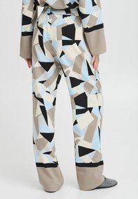 Pantalones estampados con cintura elástica, que presentan formas geométricas en azul, beige, negro y blanco. El material parece texturizado y ligero.
