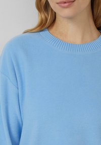 Hellblauer Pullover mit geripptem Rundhalsausschnitt und weicher Textur, drop shoulder Ärmel und einem lässigen Schnitt.