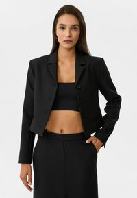 Zwarte cropped blazer met een reverskraag, enkelvoudige knopen en lange mouwen, gecombineerd met een zwart cropped top en hoge taille broek.