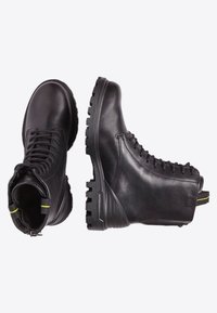 Botas de cuero negro con punta redonda, parte superior texturizada, cordones en la parte delantera y suelas de goma resistentes, con un tirador de acento amarillo en la parte posterior.
