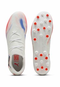 White athletic shoes with a textured upper featuring red and blue accents. The sole has six orange studs for traction. QR code visible inside.