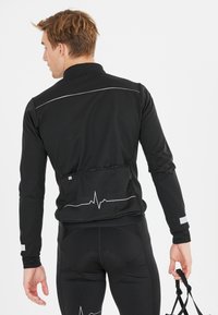 Veste de sport noire avec des accents réfléchissants, manches longues et une ligne pulsée imprimée dans le dos. Texture lisse, design ajusté.