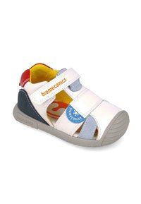 Sandal bianco con cinturini in velcro, suola in gomma grigia e accento blu; presenta un tacco rosso, interno giallo e marchio sui cinturini.