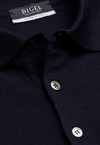 Dunkelblauses Poloshirt aus strukturiertem Strickstoff. Verfügt über einen spitzen Kragen, eine Knopfleiste mit zwei Knöpfen in Schwarz und Silber sowie einem Markenlabel.
